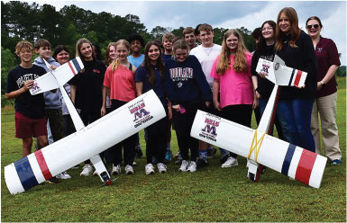 Group of students outside with model planes on grass field.