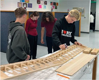 Students building wooden model in classroom.