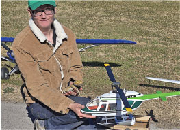 Person holding a model helicopter outside, wearing a jacket and green cap.