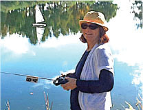 Person in hat smiling by a lake, holding a remote control.