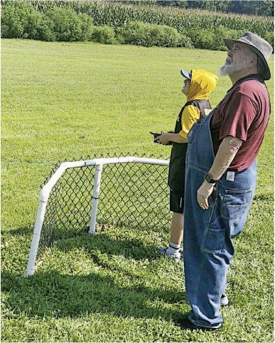 Man and boy watching, standing by small soccer goal, on a sunny field.