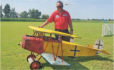 Man with model biplane on grass.
