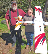 Man and child holding a large model airplane outdoors, smiling.
