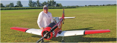Man with large model airplane on grassy field.