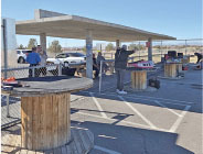 Covered parking area with people, wooden cable spools, and a sunny sky.