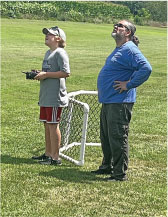 Two people look up at the sky on a grassy field near a small goalpost.