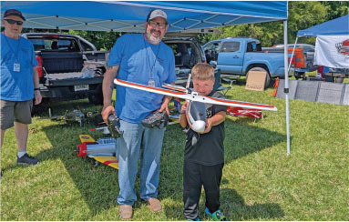 Boy and man holding a model airplane under a blue canopy.