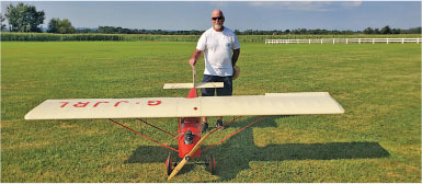 Man standing with a large model red-and-white airplane on a grassy field.