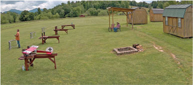 Model airplanes on stands, grassy field, wooden sheds, people seated under a canopy.