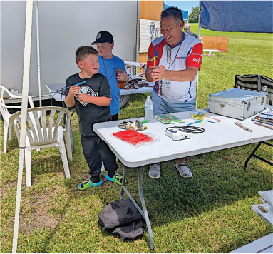 Two children and a man with rocket models at an outdoor table. Bright, sunny day.