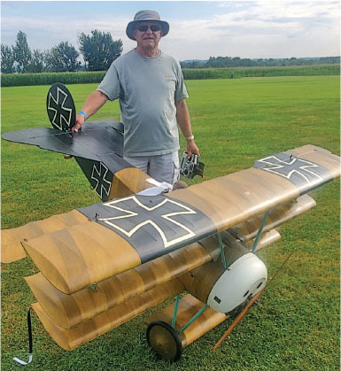 Man with model biplane on grassy field, wearing a hat and sunglasses.
