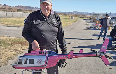 Man holding pink and white model helicopter outdoors.