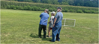 Three people standing on grass, looking toward a field, near a small goal.