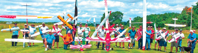 People holding model planes on a grassy field under a partly cloudy sky.