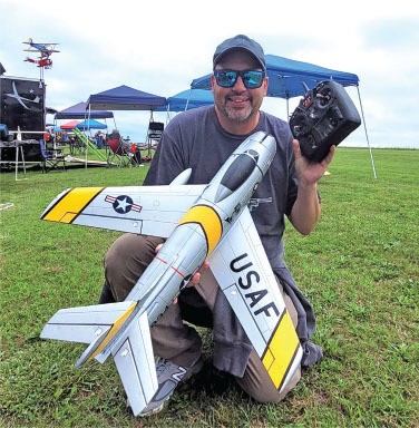 Man kneeling on grass, smiling with a model jet, marked "USAF" and a remote control.