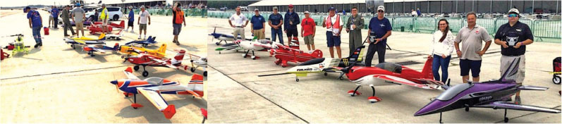 People standing with colorful model planes on a concrete airfield.