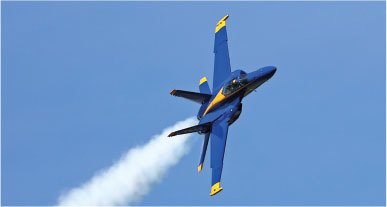 Blue and yellow jet performing aerobatics against a clear blue sky.