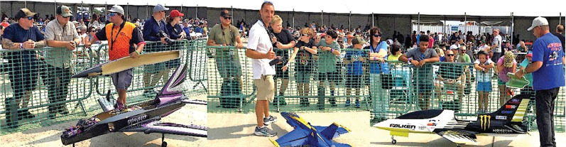 People viewing model planes at an outdoor event behind a green fence.