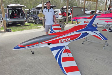 Man standing beside large red, white, and blue model plane labeled "BDX."