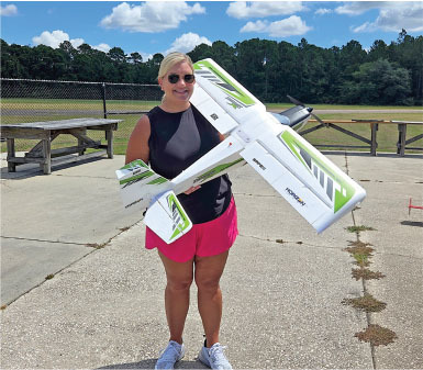 Smiling woman holds a large model airplane outdoors.