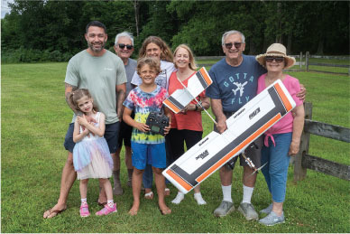 Family smiling in a field holding a model airplane.