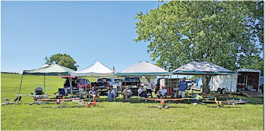 Tents and RC planes on grass under a clear blue sky.