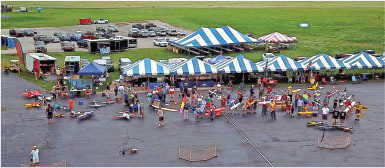 Outdoor event with striped tents, people, and colorful model planes on a concrete area.