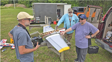 Three men examining a large model airplane outdoors.