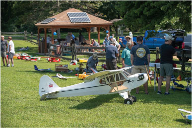 Model airplanes on grass with people gathered around, gazebo in background.