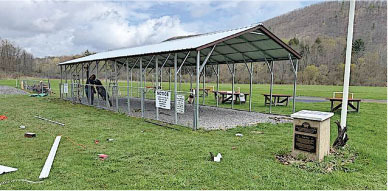 Open-sided pavilion with tables and signs in a grassy field.