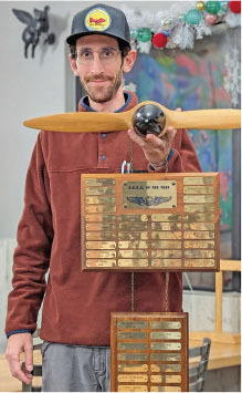 Man holding a large wooden propeller trophy with engraved plaques.