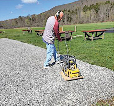 Man in headphones using a compactor on gravel path in a park.