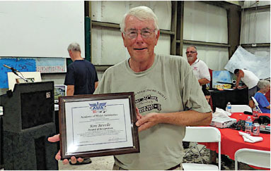 Man holding an award certificate in a room, smiling.