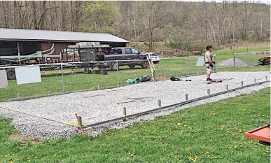 Man standing on gravel by a fence, outdoors with trees in background.