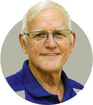 Smiling elderly man wearing glasses and a blue shirt.