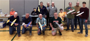 Group of people holding small model airplanes indoors, smiling at the camera.
