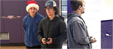 Two people control a drone indoors; one wears a Santa hat.