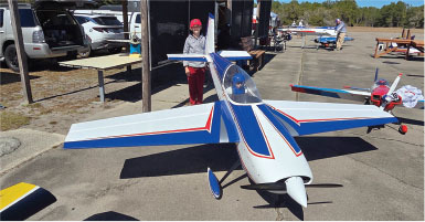 Large model airplane with blue and red stripes on tarmac; person standing nearby.