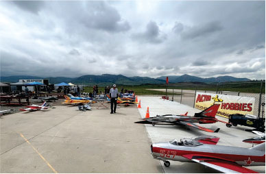 Remote-controlled planes on a tarmac with mountains under cloudy skies.