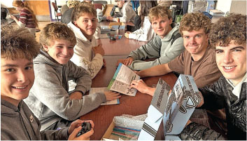 Six young men smiling around a table with books and a model plane.