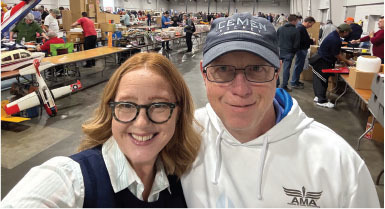 Two people smiling at a model airplane event indoors.