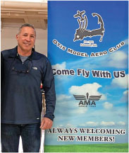 Man standing next to "Otis Model Aero Club" banner, inviting new members.