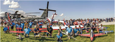Group with model planes and helicopter at a sunny air show.