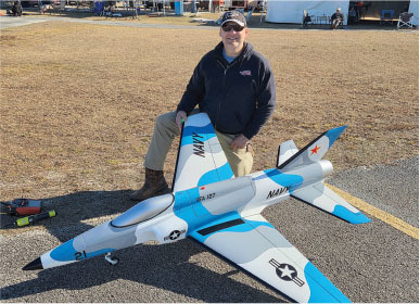 Man kneeling beside large model Navy jet on ground.