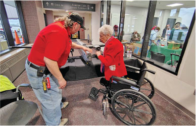 Man assisting elderly woman in a wheelchair at information desk.