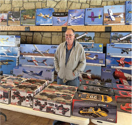 A person stands behind a table with model aircraft and car boxes.