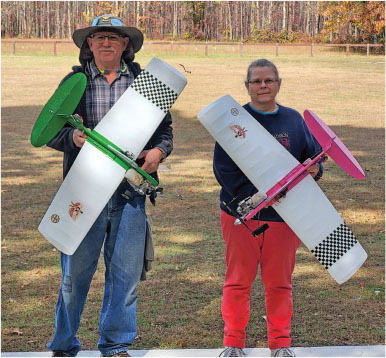 Two people holding model airplanes on a grassy field.