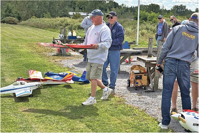 Man carrying a model airplane outdoors among several people and planes.