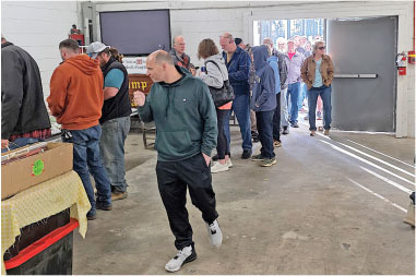 People lined up indoors, one person in foreground walking away.