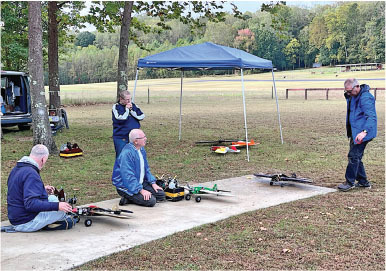 People preparing model planes under a canopy in a grassy field.